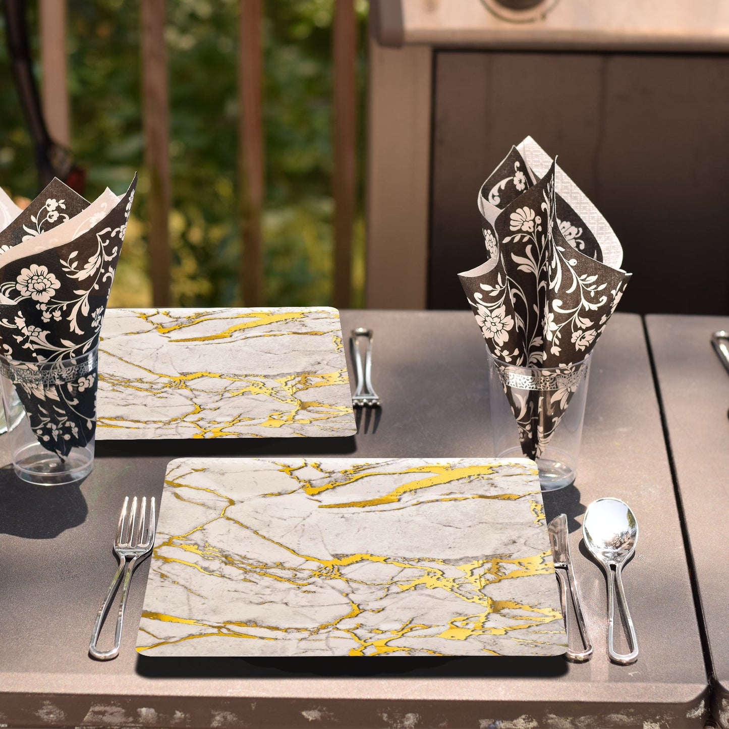 White square plates with golden marble pattern arranged for an upscale garden event with wood accents.
