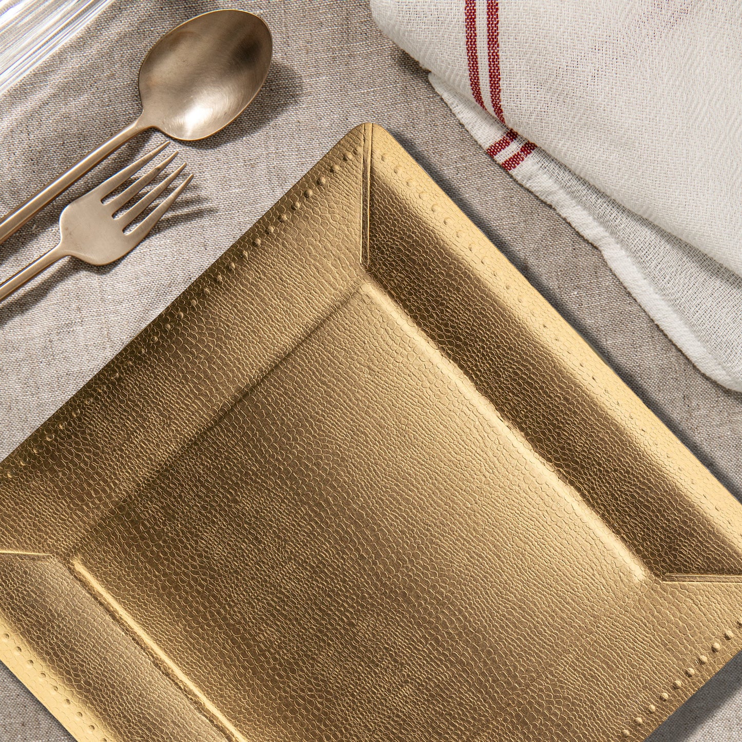 Gold beaded square charger plates styled on an elegant table with taper candles and layered place settings.
