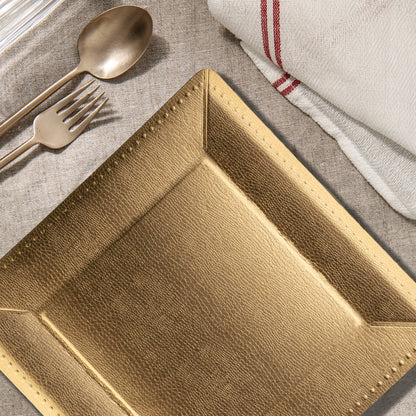 Gold beaded square charger plates styled on an elegant table with taper candles and layered place settings.