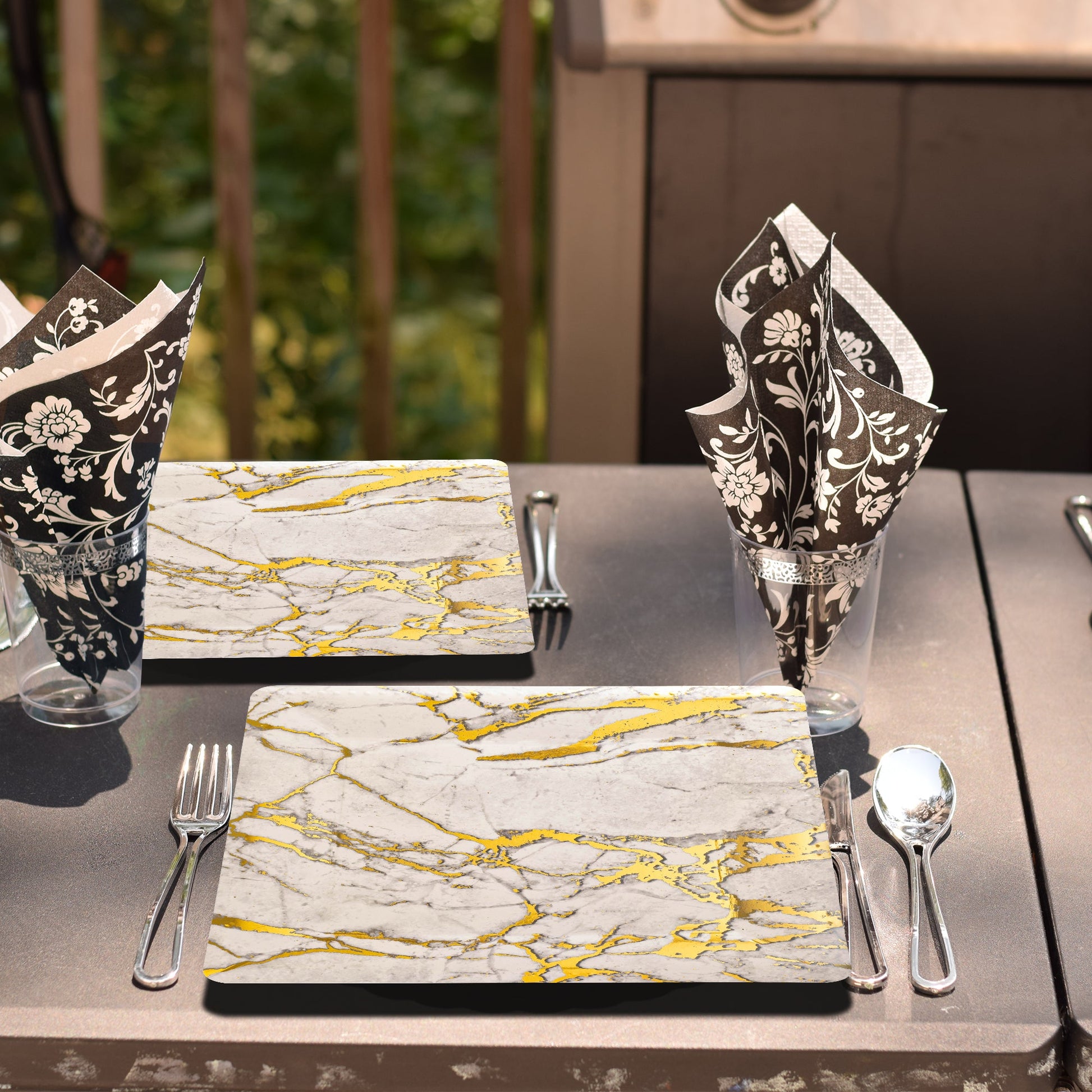 White square plates with golden marble pattern arranged for an upscale garden event with wood accents.